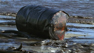 Oil drum leaking oil into sea. Drum is stranded on a beach.