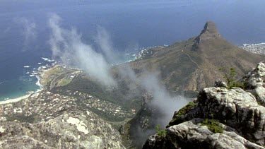 HA. View from Table mountain of Cape Town suburbs and sea below. Wisp of cloud hangs in the air below.