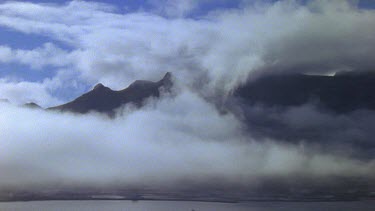 Mountain peaks stick out above low lying cloud. Wind blowing clouds.