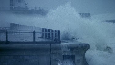 Waves crashing over boardwalk, stormy sea.