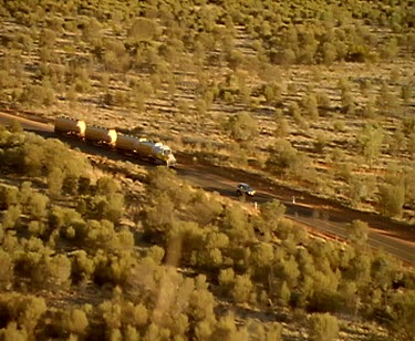 Pan high angle on petrol tanker driving along outback road. Tracking shots. Dust.  In the Outback all produce is moved by truck. These huge rigs are called road trains. This petrol tanker is more than...