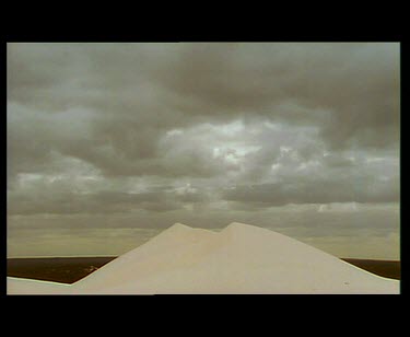 Clouds blowing over very white sand dunes. Wind blowing sand over top of sand dune.
