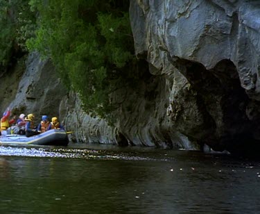 Rafting down river past rock formation overhanging water