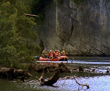 Rafting down river past rock formation overhanging water