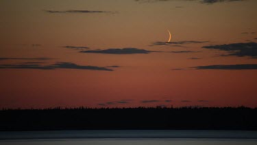 An endless Alaskan sunset makes for the perfect backdrop for the setting moon. Longest day. Land of midnight sun. Day and night contrast. Seasons.