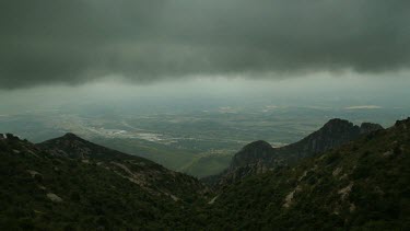 Set high on Mt Montserrat, clouds move through the camera in this scenic timelapse. Mt Montserrat is a major tourist attraction in Spain.  Dark rain clouds. In distance patchwork of fields, a highway.