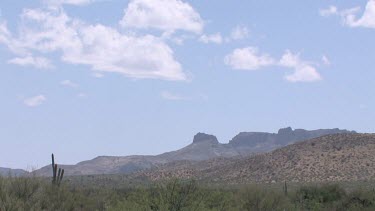 Desert valley with saguaro, desert brush, clouds, blue sky, and distant mountains