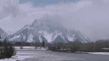 Mountains with snowy peaks, cloud cover, and fozen lake