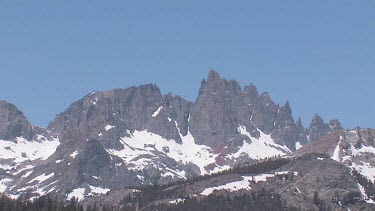 Jagged mountain peaks with snowy base, blue sky and forest