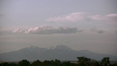 Distant mountain range with cloud filled sky and dark tree line