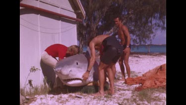 men lift and move dummy shark