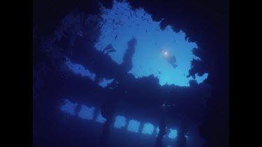 Diver swims past frame of wreck with light