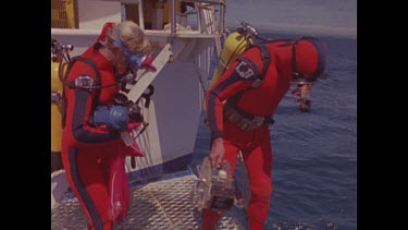 two divers in red wetsuits jump into water