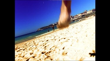 Low Angle. Two surfers jump over camera and run towards the sea. Bondi Beach.