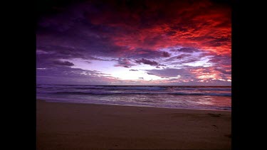 Sunrise over beach. Clouds pink and blue. A girl runs towards the sea and dives in.