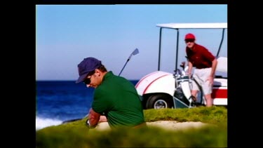 Golfer hits a shot on beach golf course. Wave crashes in background.
