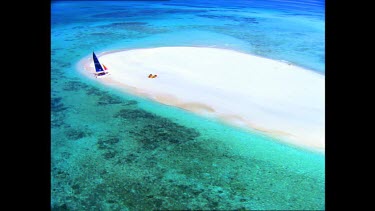 Catamaran and people on isolated sand bar in middle of reef