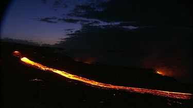 Volcano erupting. Night. Very long lava flow along a channel.