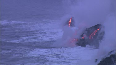 Waves crashing onto lava flow and turning into steam. Lava dropping into ocean. daybreak sunrise.