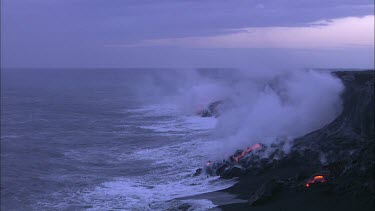 Establishing shot. Zoom in to close up Base of volcano beach, the waves crashing into the volcano and turning to steam. Birds flying. Incandescent lava. Sunrise. Daybreak.