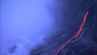 Lava flowing down narrow channel through recently solidified lava crust. Steam rising