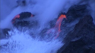Waves steam and lava flowing into ocean. Cooled lava has solidified into black rock.