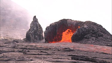 Lava bubbling through vents and flowing down channel. The lava is flowing beneath the solidified crust in lava tubes. Lava bubbles up and splashes. Eruption, erupting.