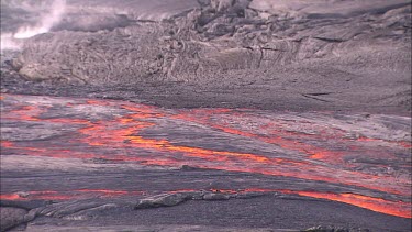 Lava flowing in channel. River of lava. Pan to where lava bubbles and erupts from a vent.