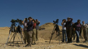 Birders watching bird migration and looking through binoculars above eilat mountains