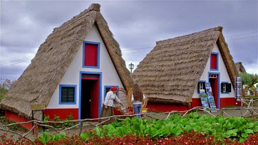 Local Woman & Tourist At Traditional Thatched Triangular Houses, Santana, Madeira, Portugal